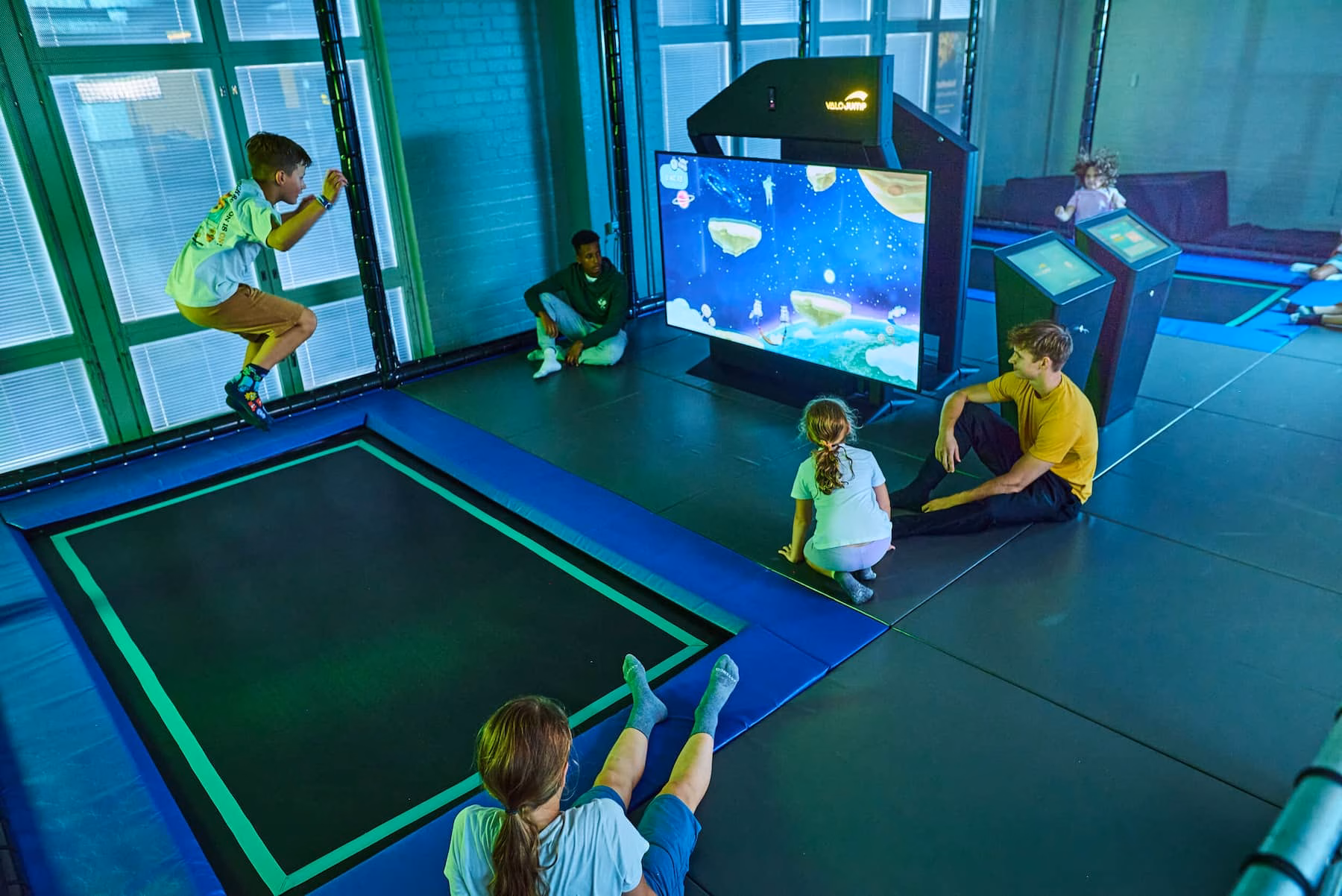 Kind springt auf interaktivem Valo Jump Trampolin mit Bildschirmspiel, während weitere Kinder und ein Betreuer im Jungle Adventures Funcenter Peine zuschauen und warten